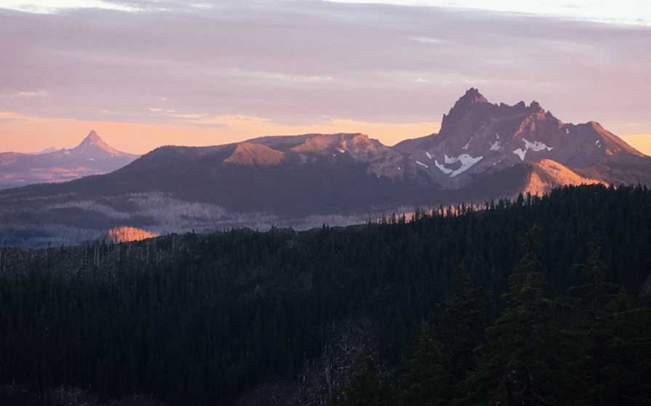 a vast mountainous landscape appears purple and pink from the sunrise or sunset